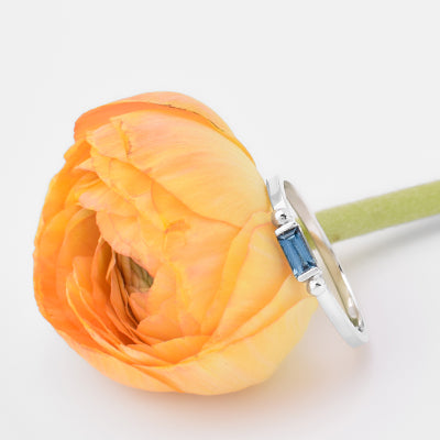 minimalist silver baguette gem ring next to a yellow flower with white background