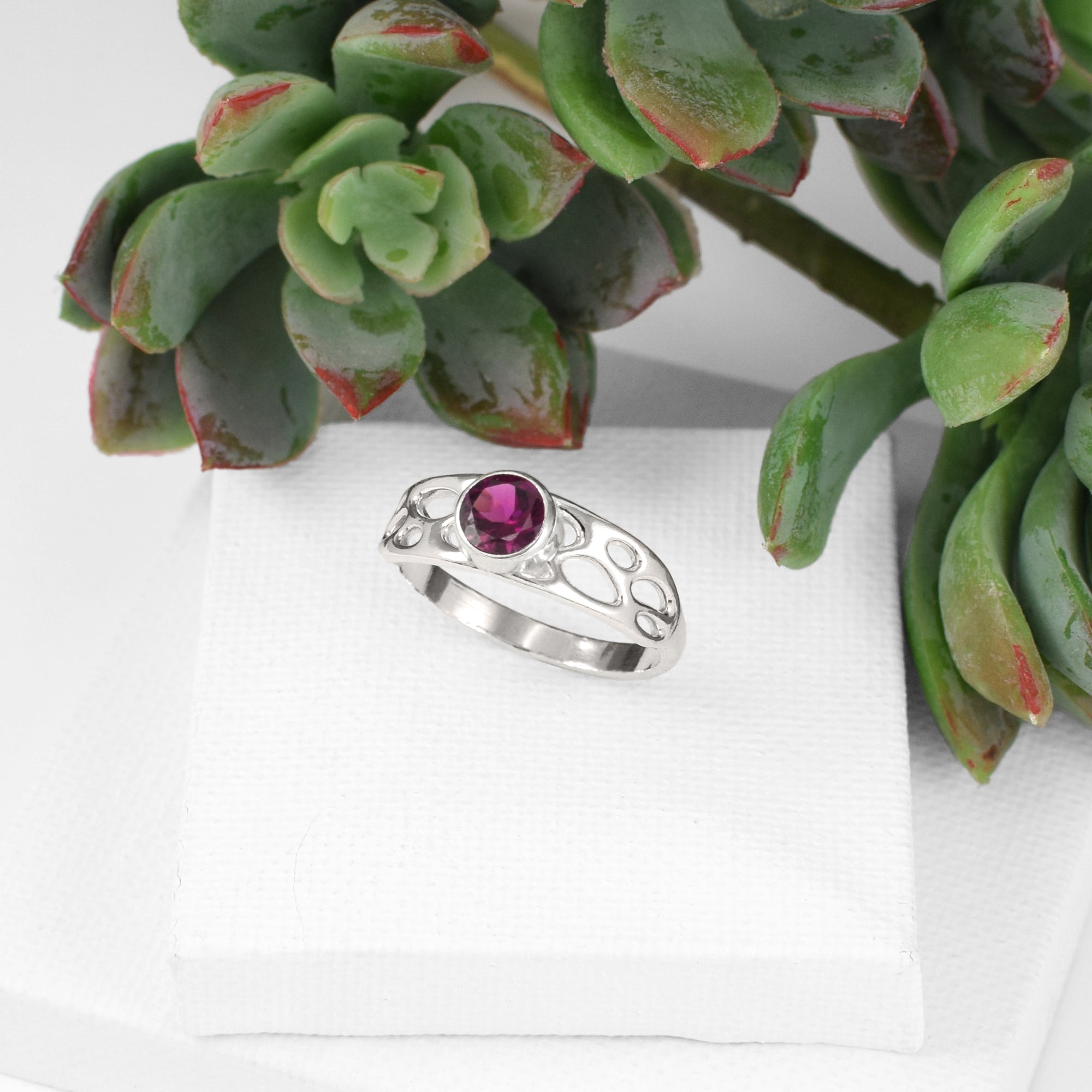 botanical solitaire ring with garnet on white background with plant