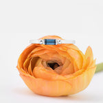 nature inspired silver ring with topaz baguette on top of a yellow flower with white background
