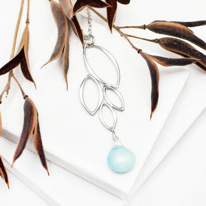 Image of silver four leaf necklace with aqua chalcedony gemstone on white blocks with brown plant.